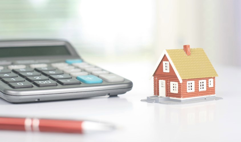 Close up of a small house ornament next to a calculator